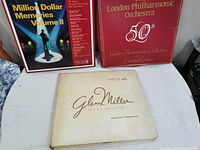 Photo showing three main items on a table: Readers Digest Million Dollar Memories Volume II LP set box, London Philharmonic Orchestra 50th Anniversary 5 LP set box, and a Glenn Miller book titled 'Second Pressing'. All items show some wear and tear.