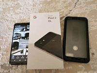 Google Pixel 2 XL smartphone powered on, displayed next to its original box and a black waterproof case with clear front panel.