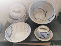 Four pieces of pottery displayed together include a bean pot with lid, large bowl, medium bowl, and butter dish with lid. All are beige with blue decorative swirls and a speckled finish.