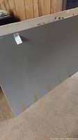 Large gray painted surface with some paint marks and stains, photographed on carpeted floor against wood panel wall.