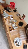Wide shot of dresser top displaying various jewelry pieces, trinket boxes, and small containers including a wooden box, different styles of earrings, necklaces, pins, and small bowls.