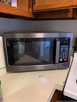 Front angled view of Toshiba EM131A5C-BS microwave oven on kitchen countertop, showing stainless steel body, black window, and digital control panel with display at 0:00