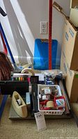 Photo of the collection of office supplies including tape dispenser, stapler, hole punch, yardstick, clipboard, and boxes.