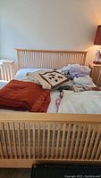 Queen bed frame with mattress and linens piled on top; visible headboard and footboard with vertical slats