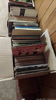 Overhead view of cardboard box containing two rows of assorted vinyl LP sleeves