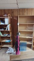 Two wooden bookshelves side by side in basement against wood panel wall. One is taller with multiple fixed shelves, the other is shorter and foldable with two stacked shelves.