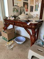 Front and side view of ornate carved wooden sideboard with various ceramic and glass items on top and below. Shows overall condition and scale.