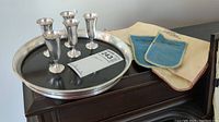 Six sterling cordial glasses arranged on round serving tray with polishing cloths to side
