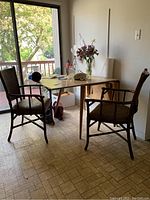 Photo showing the drop leaf table with two wicker-like armchairs beside it, placed near a sliding glass door with outdoor deck visible.