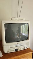 Photo shows front view of Zenith TV/VCR combo unit with 13-inch screen and remote control on top, sitting on wooden furniture.