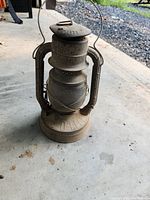 Front and side view of complete antique Dietz D-Lite No 2 lantern showing metal frame, glass globe and carrying handle on concrete floor.