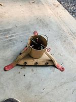 Full view of antique metal Christmas tree stand with three legs and integrated electrical cord.