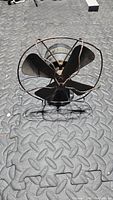 Front view of Sears Arctic antique miniature fan showing the four metal blades and protective wire cage, placed on a textured metal surface.