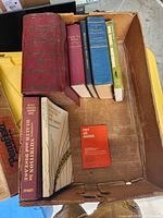 Full view of 7 old books in a cardboard box, showing titles and spines clearly visible.