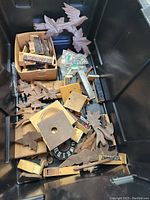 Black bin filled with assorted wooden cuckoo clock parts including bird carvings, clock faces, and leaf decorations.