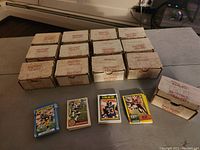 Thirteen factory boxes stacked with the text 'FACTORY SEALED' printed on them. Four opened stacks of football cards in front featuring Eric Dickerson cards from multiple years.