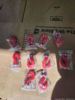 Ten red grab hooks individually wrapped and laid out on cardboard surface in sunlight.