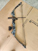 Photo showing the full compound bow laid on cardboard, highlighting the shape, cam system, and mounted sight.