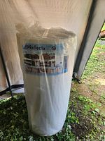 Roll of Reflectix insulation wrap in original plastic packaging showing full roll standing upright inside a tented or covered area.
