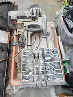 Top view of the Rigid tile saw showing the sliding cutting blade unit and orange plastic water tub below, dusty and worn.