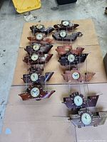 Multiple skipper clocks displayed on floor, designed as wooden boats with round clock faces and metal masts.
