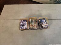 Image of three separate piles of sports cards sitting on a white table, mostly baseball cards with some sleeved in clear protective plastic.