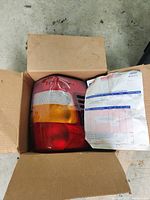 Tail light assembly inside a cardboard box showing amber, red, and clear lens sections.