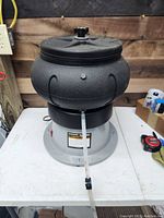 Black vibratory bowl parts cleaner on gray base with clear plastic tube attached.
