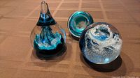 Three Caithness glass paperweights on a table: Hershey kiss shape, Splashdown, and Millennium. Shows overall size and shape of each item.