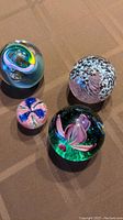 Four round glass paperweights with distinct artistic designs, placed on table showing colors and shapes.