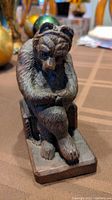 Front view of hand carved wooden bear figurine sitting with legs crossed on base.