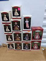 Photo showing 14 Barbie Keepsake Collector's Series ornaments in original boxes arranged on cardboard, including multiple designs with elegant gowns and holiday dresses.