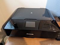 Front and top view of black Canon printer with touchscreen and control buttons.