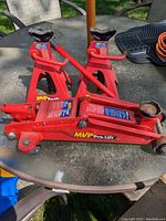 Three red MVP Pro-Lift automotive tools placed on a round outdoor table: one hydraulic floor jack and two jack stands. Shows general condition and color.