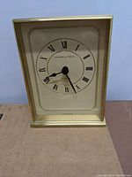 Front view of Hamilton clock showing gold-tone metal frame, Roman numeral dial, and black clock hands.