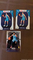Three rookie basketball cards displayed on brown surface: two LaMelo Ball NBA Hoops cards with teal Charlotte Hornets uniforms and one Ja Morant Panini Prizm card in light blue Memphis Grizzlies uniform.