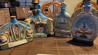 Four blue-toned collectible ceramic decanters with raised-relief Kentucky Derby themed artwork on kitchen table.