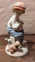 Side view of the porcelain figurine showing the boy seated with dog beside him, wearing pastel clothing and cap.