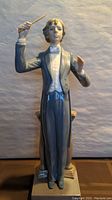 Front view of full figurine showing conductor in gray tailcoat with raised baton