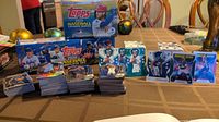Wide view showing three piles of basketball rookie cards, baseball card boxes and football cards stacks on table.