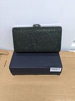 Front view of rectangular pewter-colored crystal evening clutch bag on a black box.