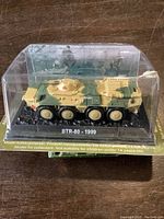 Side view of diecast BTR-80 model in original display case showing camouflage colors and detail.