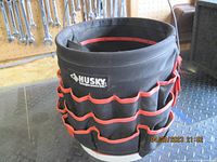 Front and side views of black Husky jockey pouch with red trim mounted on white plastic pail, showing multiple pockets and loops.
