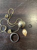 Photo showing all jewelry items on a dark wooden surface including chain necklace with spherical pendant, religious medallion, silver ring, heart pendant, and earrings.