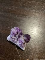 Photo of a natural amethyst cluster showing multiple purple crystal points and a white base on a wooden surface.