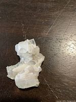 Photo of natural clear crystal stone cluster on dark wood surface showing white and translucent crystal facets.