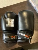 Front view of pair of black Drako boxing gloves showing brand logo on wrist strap and general condition.