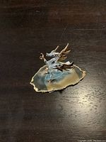 Small glass dragon figurine with 24 KT gold accents on its wings, horns, and claws seated on a polished slice of agate with gold edges, viewed from the front.