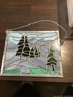 Front view of stained glass panel showing pine trees and landscape design with hanging chain