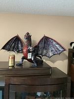 Wide view of the entire dragon figurine on a dark surface with a soda can for scale, showing its large wingspan and overall form.